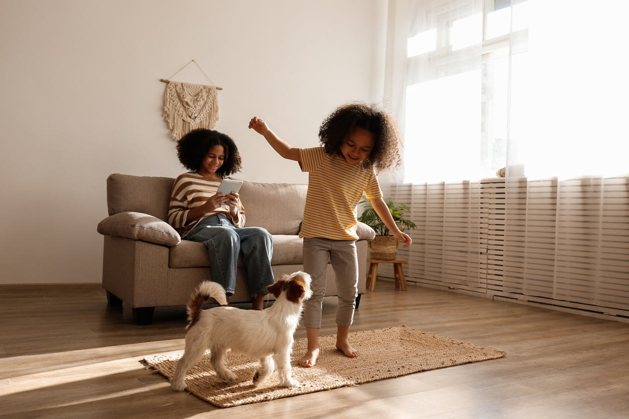 Child playing with dog on durable luxury vinyl plank flooring while mother relaxes on sofa in a bright family living room.