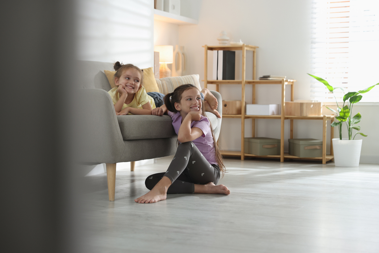 Two children relaxing in a bright living room with light luxury vinyl plank flooring, designed for family-friendly durability.