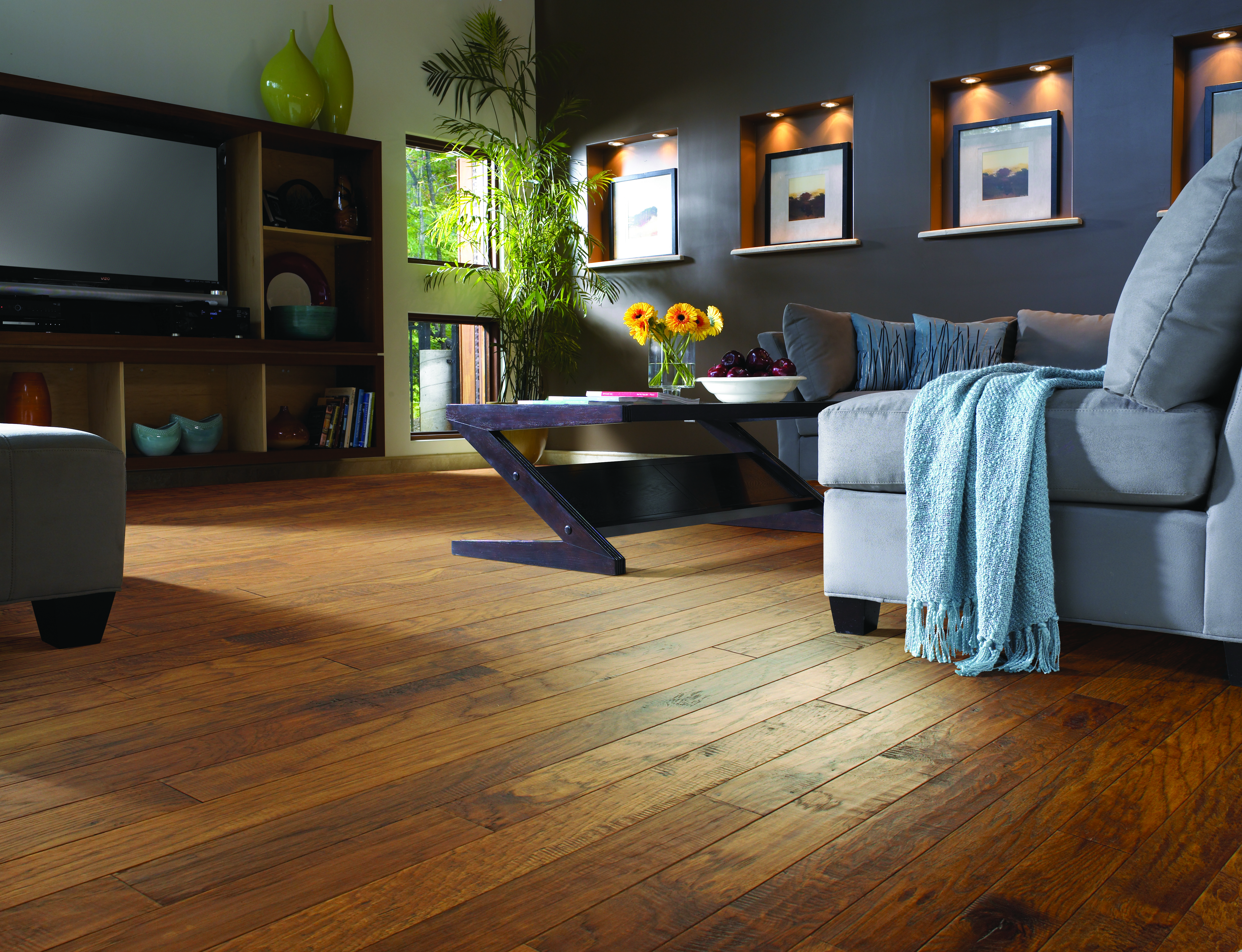 Stylish living room with warm hardwood flooring, modern grey sofa, and natural light, showcasing durable and elegant flooring design.