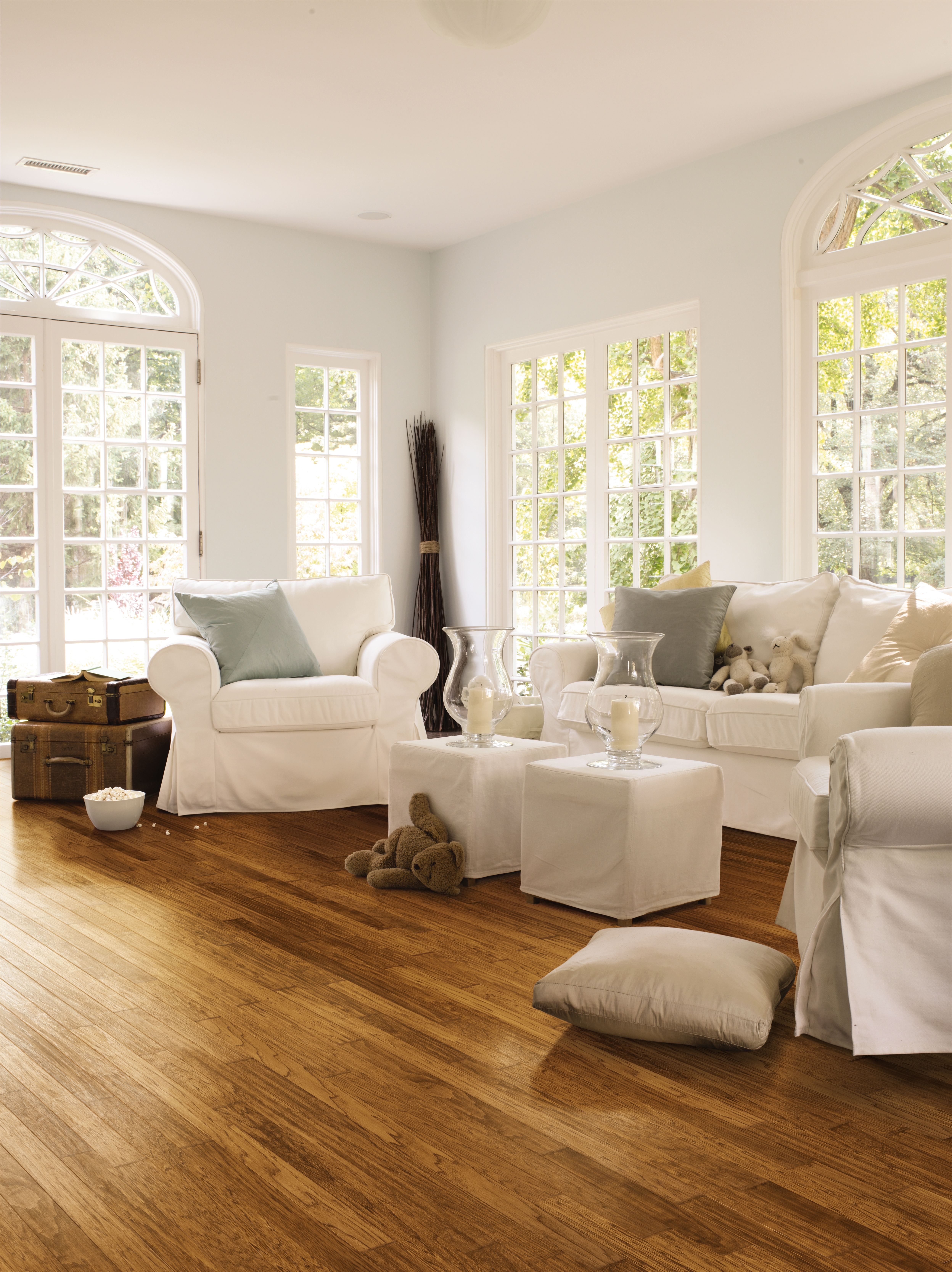 Bright living room with natural light, golden hardwood flooring, and white furniture creating a warm and inviting space.